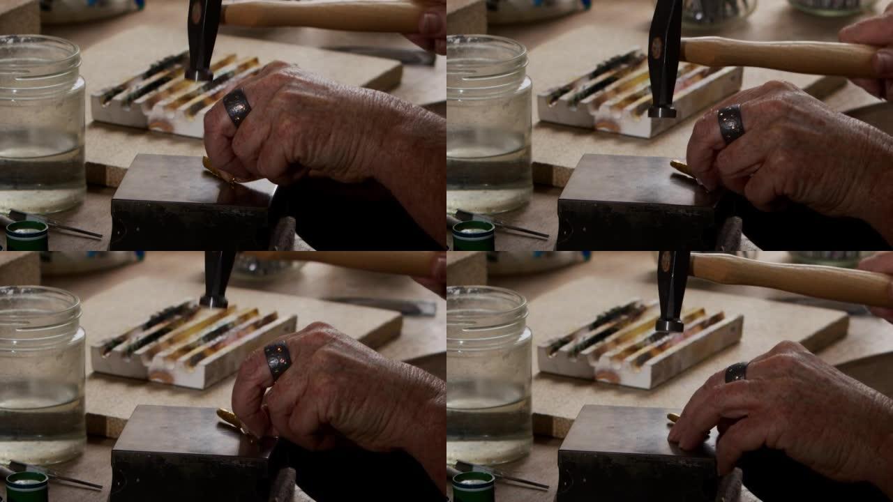 一只老年女性手的特写镜头用锤子给金锭打形状