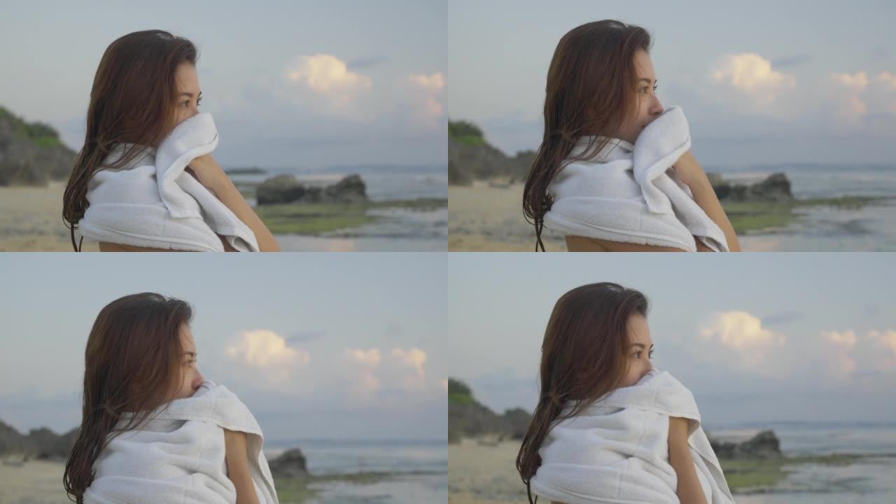 这位年轻的日本女子正在海滩上观看日落，同时裹着浴巾。