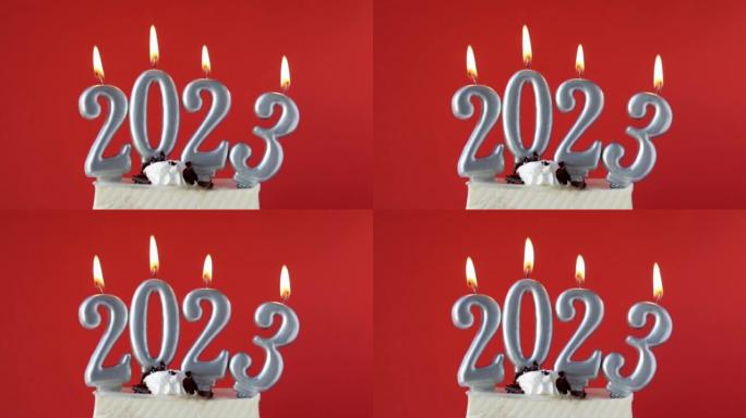 快乐新2023年数字蜡烛红蓝背景杉树圣诞装饰背景。女性手工点燃蜡烛配火柴，蛋糕切片寒假