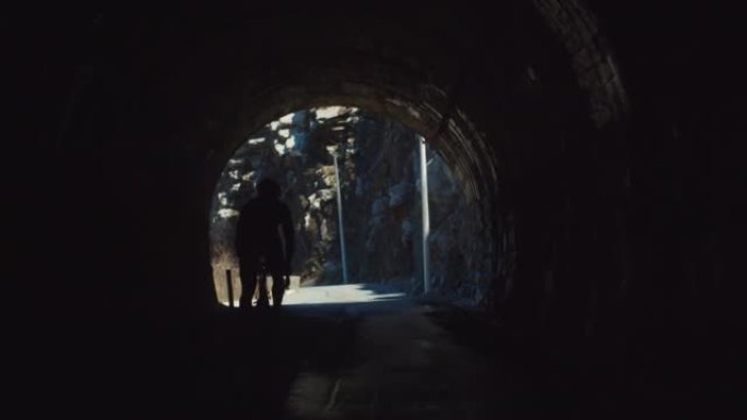 一名专业自行车手的剪影在山间隧道中，从黑暗的隧道通往光明的道路
