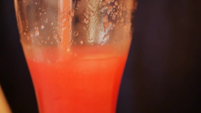 详细。玻璃与红西瓜饮料与果肉和冰，可重复使用的玻璃管。一个人喝了西瓜饮料，然后用吸管在玻璃杯中搅拌。