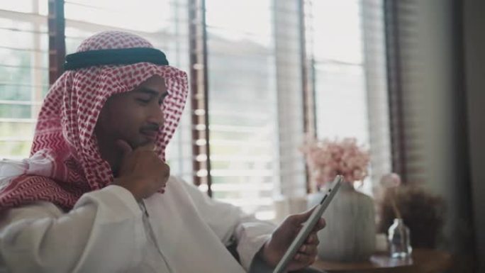 阿拉伯商人在家坐在客厅时使用笔记本电脑工作。