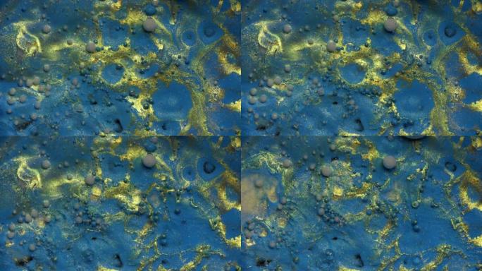 彩色油漆气泡，金色灰尘散布在蓝色水彩表面上，破裂并混合在抽象设计中。黄色闪闪发光的颗粒，墨球滴和混合