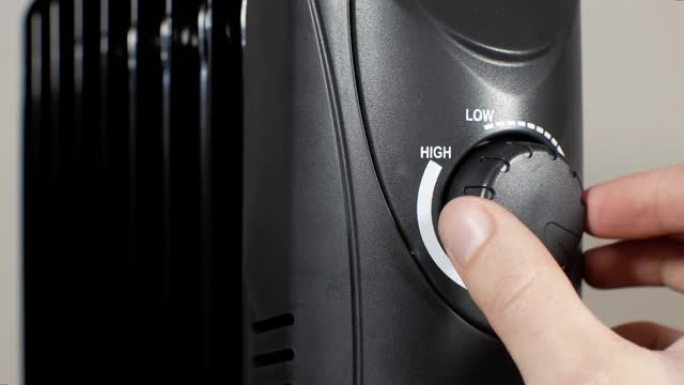 男人正在家里调节取暖油电散热器。“高” 或 “低” 调谐模式。家庭供暖和保温的概念。黑色充满油的加热