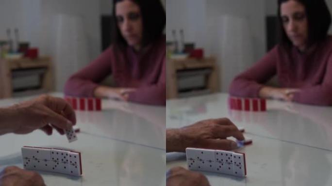 老人的手在木板上放一块多米诺骨牌，与年轻女子对战。多米诺骨牌是一个令人兴奋的古老棋盘游戏。垂直视频