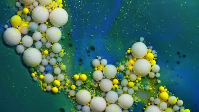 彩色金色和黄色丙烯酸涂料气泡散布在蓝色表面混合在抽象设计中。闪闪发光的灰尘，墨球滴和混合。运动中的多