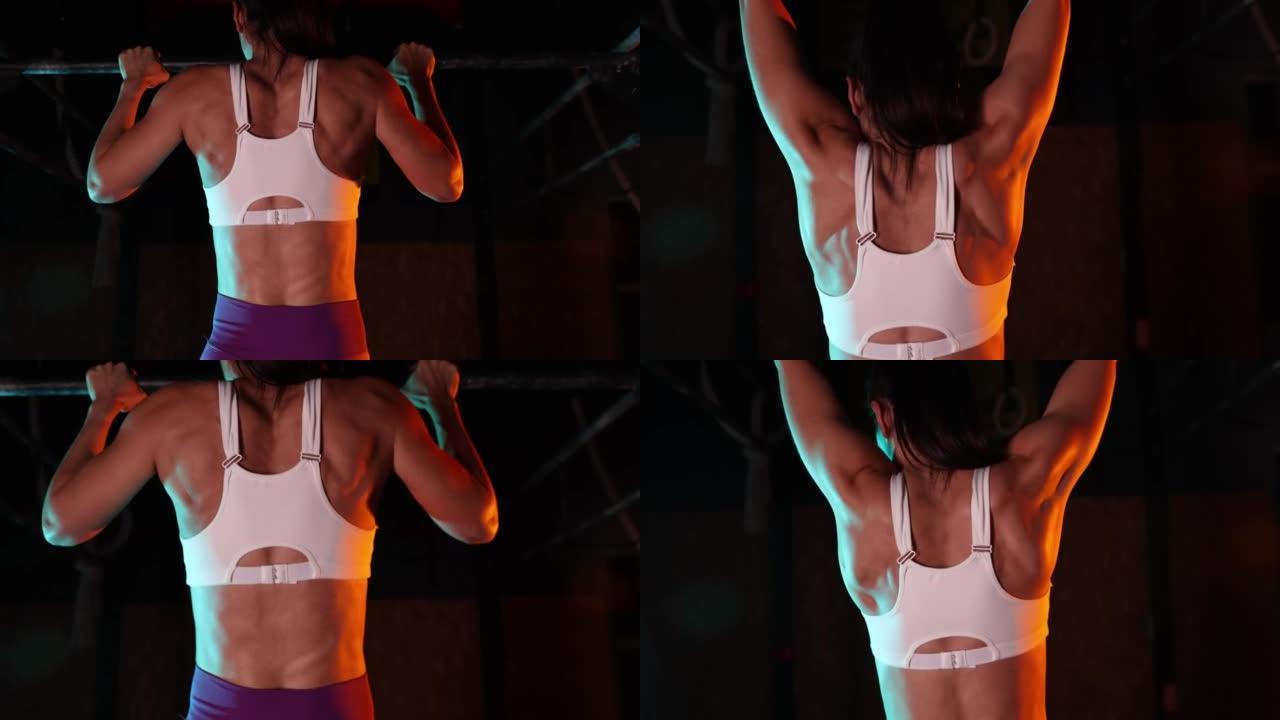 肌肉女人在霓虹灯滤光片的运动健身房的酒吧里做引体向上的特写镜头。力量和有氧运动。后视图
