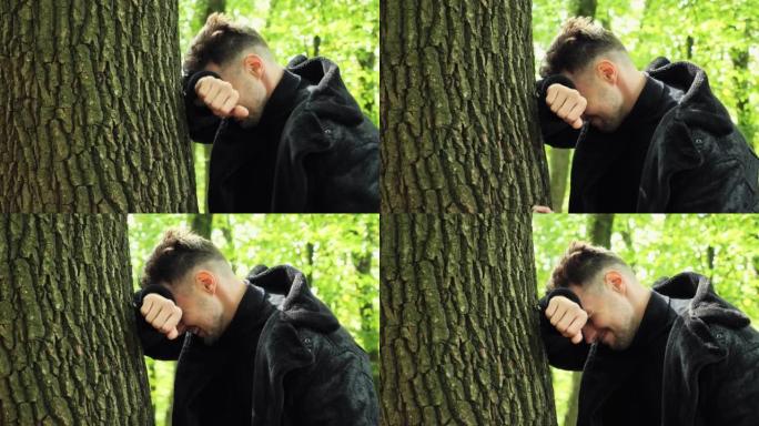 特写沮丧的男性脸悲伤的压力男人站在树林里的户外抱着头，因为深深的沮丧而哭泣，冒犯了面部表情担心麻烦问