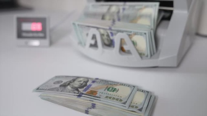 桌上摆着一串100美元的钞票。现金计数机在背景下计数100美元的钞票。特写。