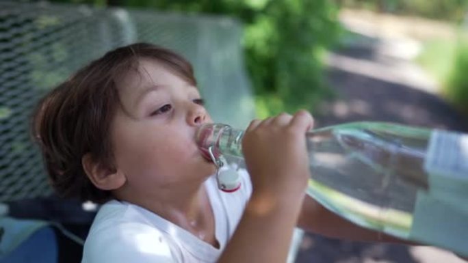 孩子在炎热的夏天喝水。小男孩在户外公园从玻璃瓶补水液体中吞咽