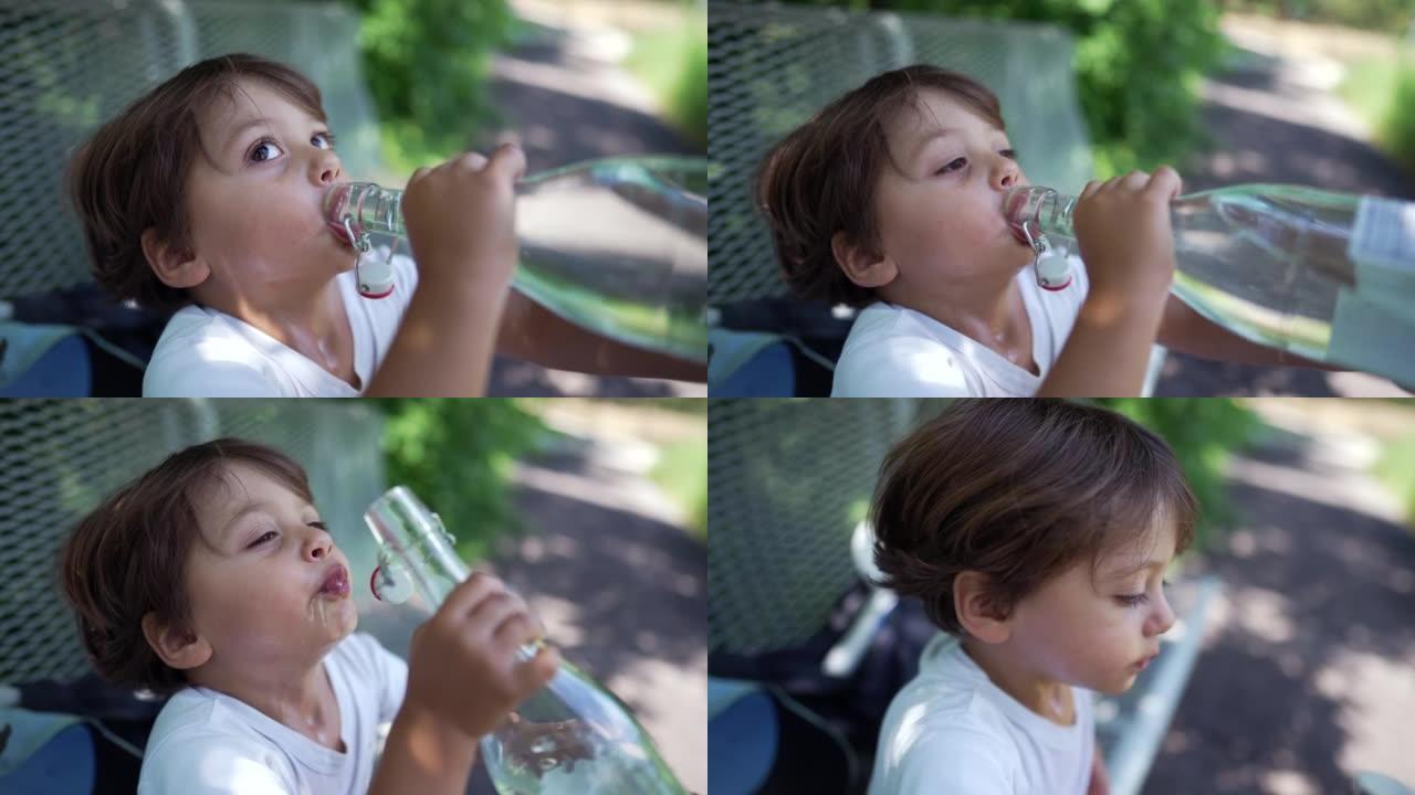 孩子在炎热的夏天喝水。小男孩在户外公园从玻璃瓶补水液体中吞咽