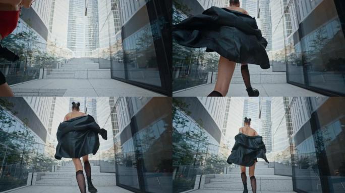 穿着黑色皮夹克和短裙的时尚女孩在现代城市中心的高层玻璃建筑旁边爬上楼梯。时尚女性，夏日，慢动作