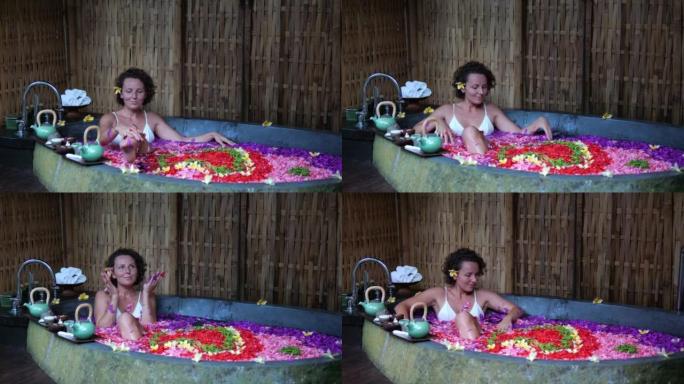 度假的女人在天堂岛的巴厘岛度假的浴室里用花洗澡。花洗澡的美女在水疗酒店放松。芳香疗法概念。