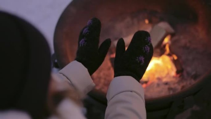 女人在壁炉附近的手套里暖手。在舒适的壁炉附近休息的女人的后视图