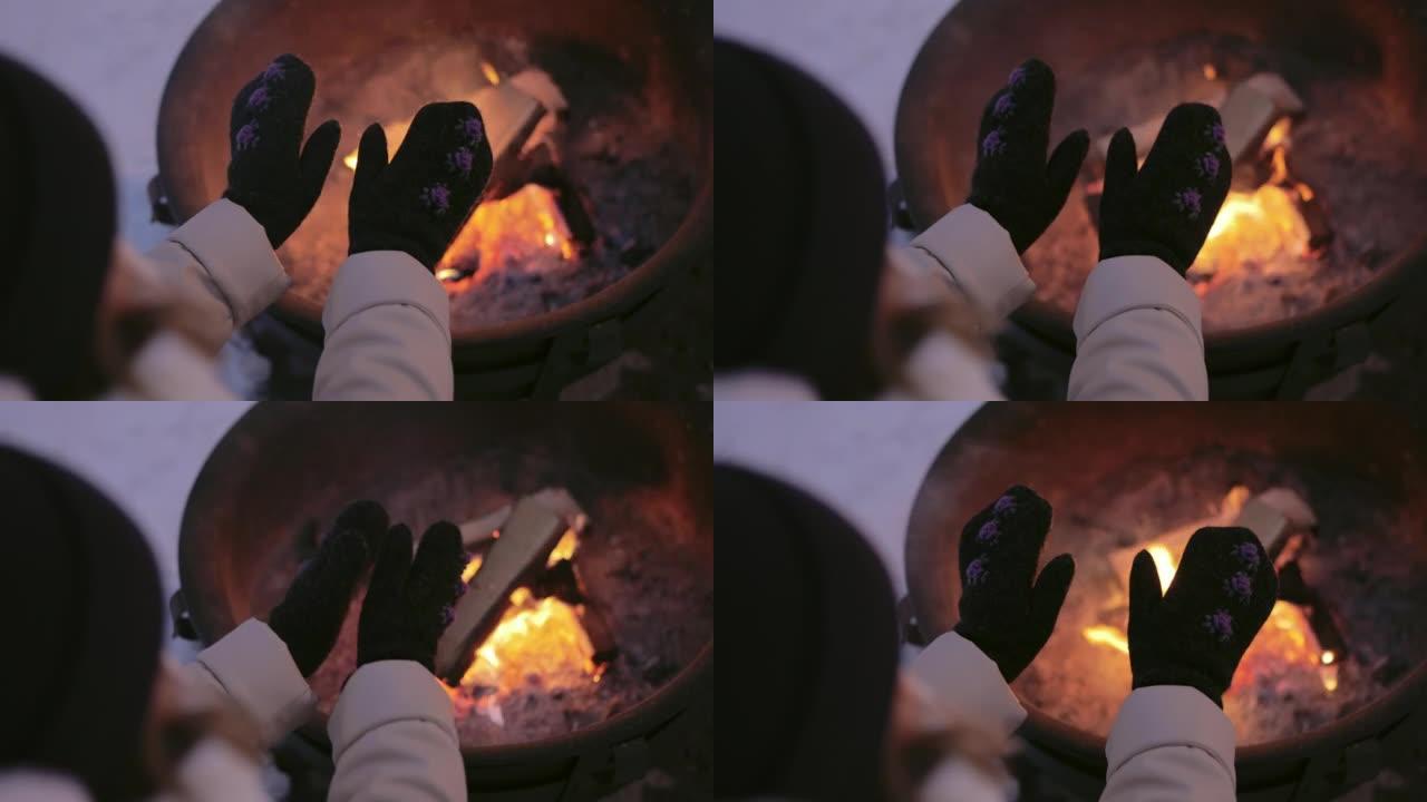 女人在壁炉附近的手套里暖手。在舒适的壁炉附近休息的女人的后视图
