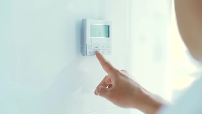 特写男人的手控制并按下按钮公寓和办公室的空调和供暖控制面板位于白色的墙壁上。