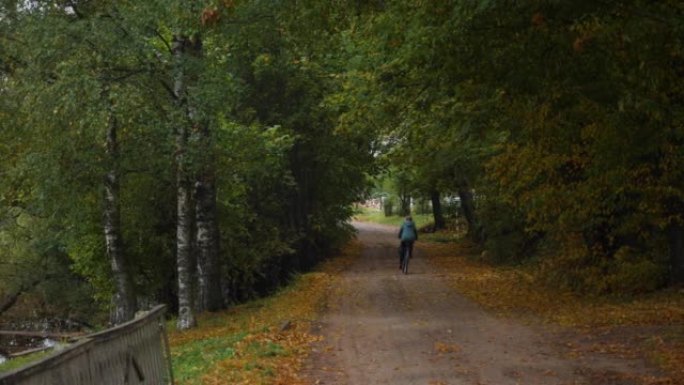 秋天，一个人骑着自行车穿过一个村庄，在秋天的雨中，在五颜六色的树之间。