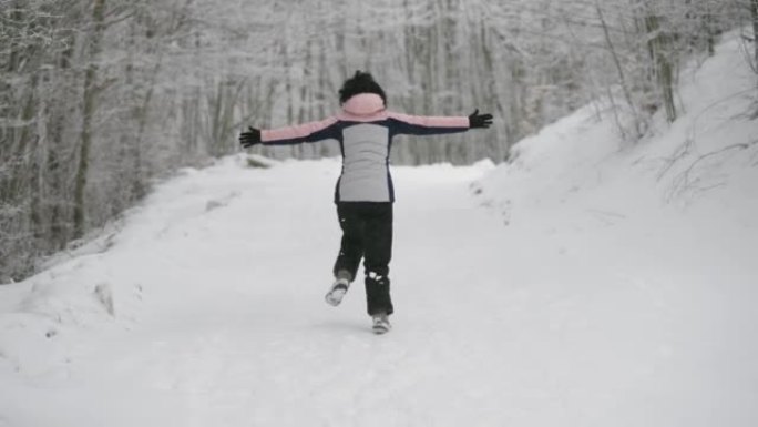 快乐的年轻女徒步旅行者在寒冷的雪中慢跑，双手张开，慢动作，后视图