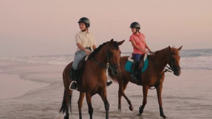 3名穿着马术服装的骑手在日落时分骑着马在海上小跑的4k视频。