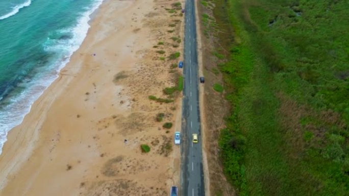 蜿蜒的沿海公路的4k鸟瞰图接近美丽的海滩，那里有海浪和碧绿的水。金色的沙滩和岩石是一个完美的夏季目的