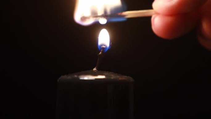 男人的手在深色背景上使用火柴点燃黑色石蜡蜡烛。明亮的火焰，火，点火。记忆、仪式、庆祝、电力问题、能源