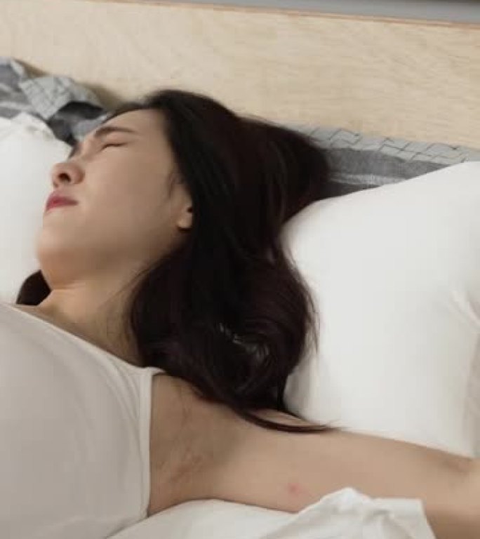 垂直屏幕: 疲惫的韩国女孩不情愿地醒来闹钟，在清晨在家试图停止床上的铃声后转身入睡