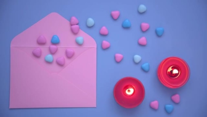情人节的背景。从上方观看。粉色信封和五颜六色的心。红色的蜡烛在燃烧，蓝色的背景。用爱的宣言创造情人节
