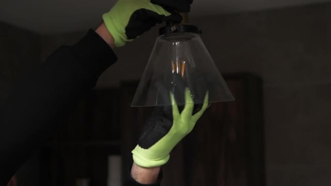 一名戴着特殊工作手套的男子正在将一盏灯拧在现代吸顶灯附近。