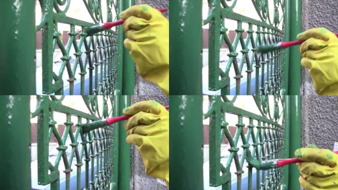 工人戴着黄色手套，保护性，用刷子刷短，用绿色油漆的铁艺围栏