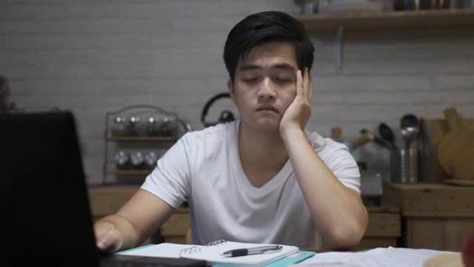 沮丧的亚洲男性在用计算机做生活费用的文书工作时感到绝望，感到担心家里饭厅的钱问题。