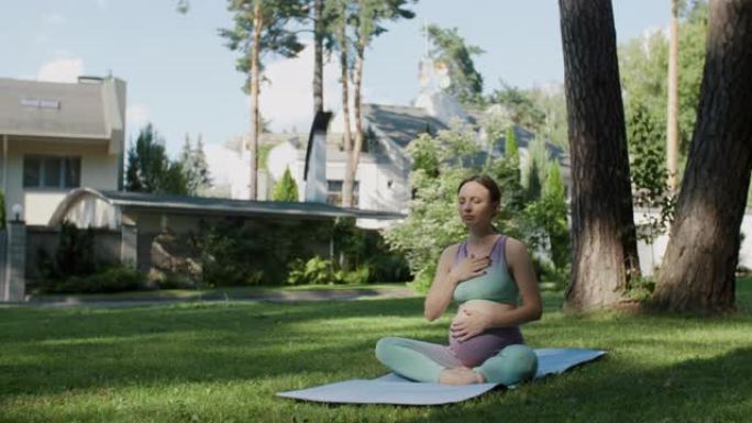 做瑜伽的孕妇坐在莲花的位置用手在怀孕的肚子上练习呼吸练习