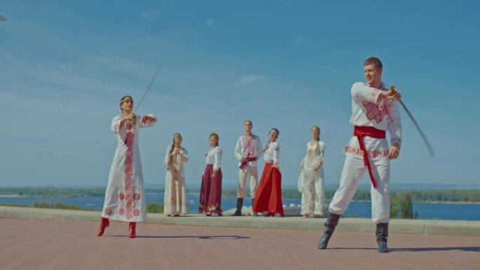 乌克兰人在河边用军刀侧翼。穿着漂亮民族服装的乌克兰男人和女人穿着军刀。美丽的女人挥舞着军刀，侧翼，历