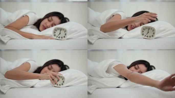 美女早上在床上被闹钟吵醒。年轻的亚洲女人不想醒来，也不喜欢闹钟的声音。