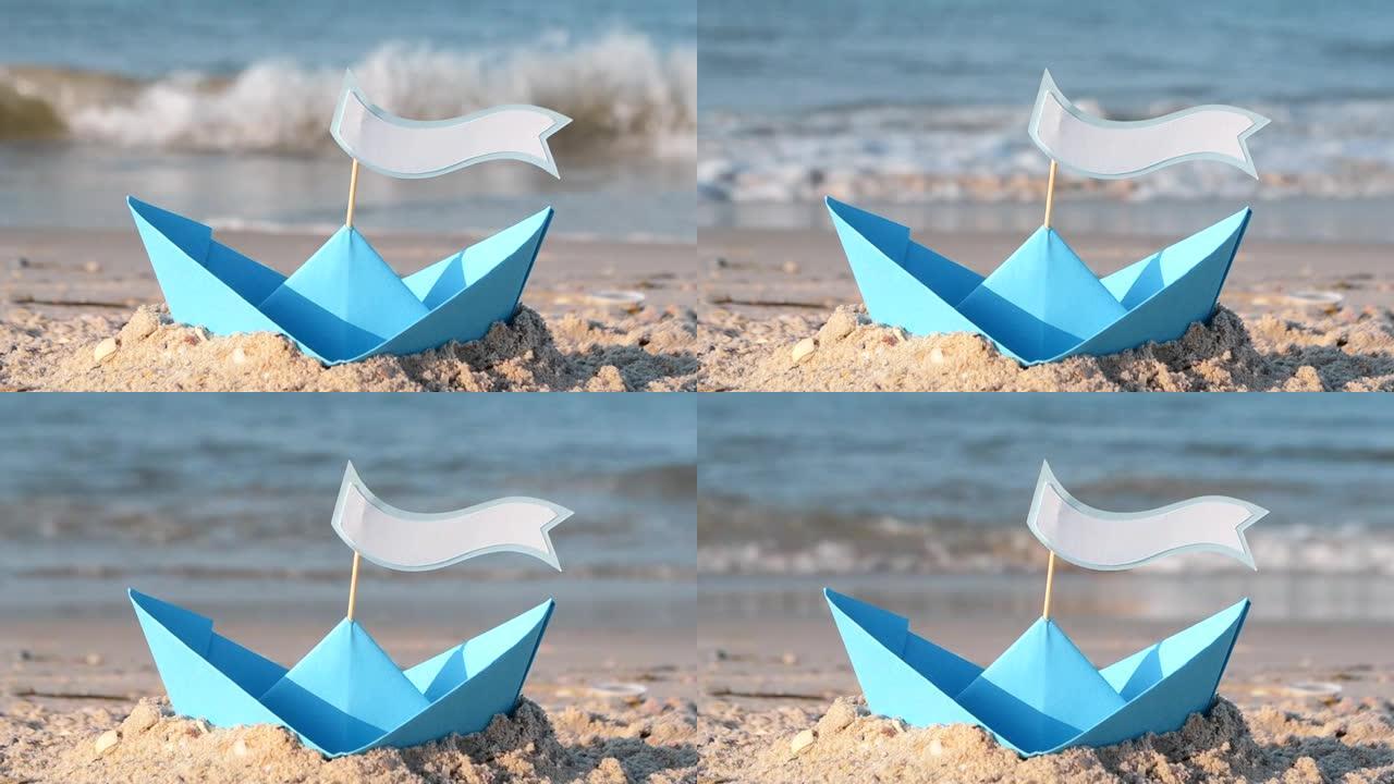 在阳光明媚的夏日，蓝纸船在海边的沙滩上。在船上，有文字空间。海浪附近沙子上的小船。概念旅行，旅游，度
