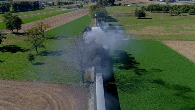 从蒸汽火车正上方的鸟瞰图，当无人机穿越乡村时，它在无人机上吹着烟雾和蒸汽