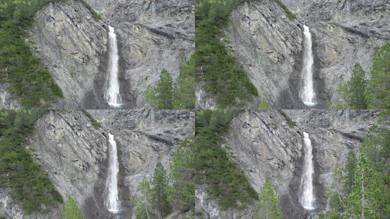 空中无人机镜头缓慢下降到树冠上，同时面对着陡峭的瀑布，它在瑞士陡峭的山崖边缘上层叠而出。