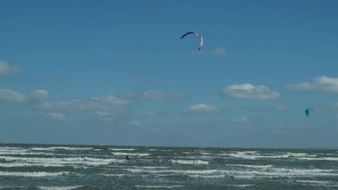 一名穿着潜水服、带着降落伞的男子在海浪上冲浪。一个年轻人顶着天空在空中表演魔术。水上运动，风筝冲浪，