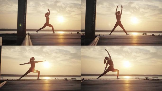 年轻的女性做瑜伽在日落时多云的天空下在码头上摆姿势 “战士”