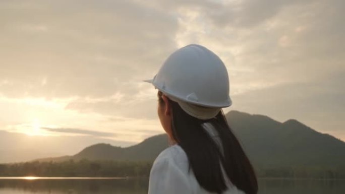 女工程师勘察大坝工地发电。穿着白色头盔的自信女建筑师看着大坝建筑工地。清洁能源和技术概念。