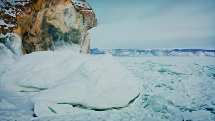 贝加尔湖，飞过破碎的冰，蓝色的雪驼峰。摄像机升起，露出山脉的景色。美丽的冬季风景。俄罗斯西伯利亚贝加