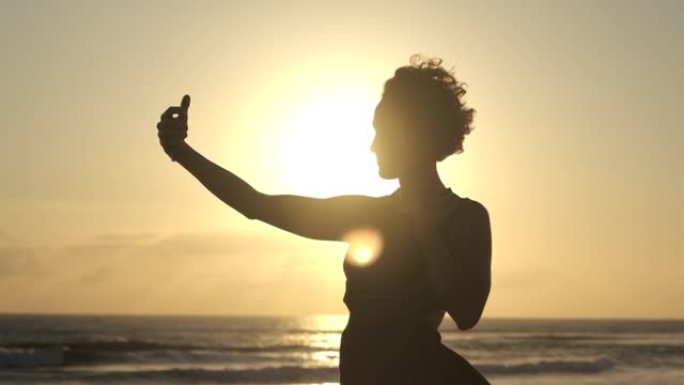 白人妇女站在地平线上落日的最后一道明亮的光线中，摆姿势对着镜头，想为她的博客拍摄美丽的照片。