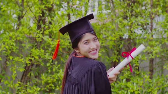 穿着帽子和礼服的迷人亚洲女学生毕业，手持证书庆祝，在毕业典礼上感到骄傲，祝贺学生毕业，教育成功