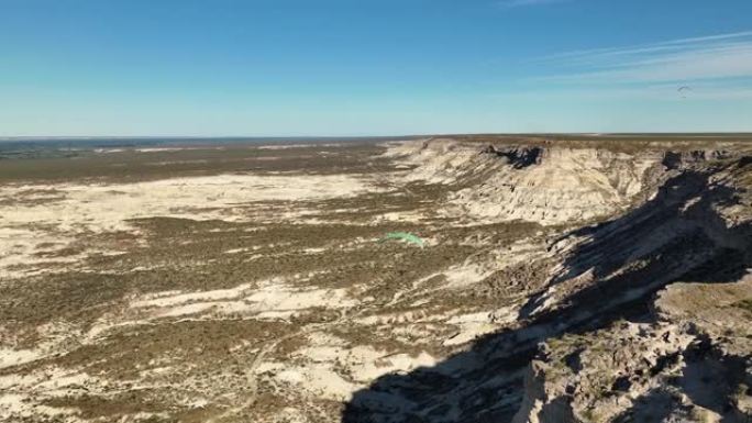 两只滑翔伞在沙漠地区上方远处飞来飞去，悬崖很大。