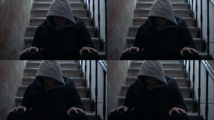 孤独的人低着头坐在黑暗中的楼梯上。压力和抑郁心理问题概念