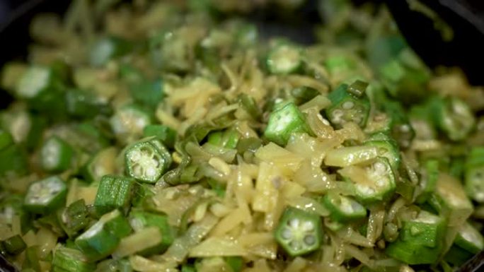 新鲜的秋葵切片与炒洋葱和土豆混合在平底锅中。特写，慢动作