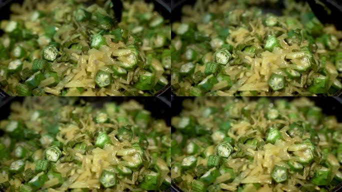 新鲜的秋葵切片与炒洋葱和土豆混合在平底锅中。特写，慢动作
