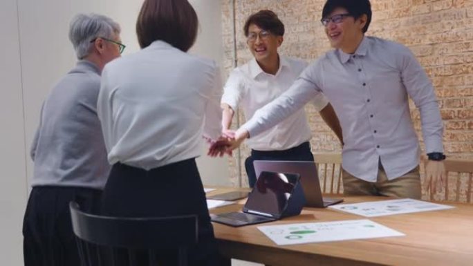 一群亚洲创意商业人士叠手将手掌放在一起。员工团队人员在办公室会议室形成手堆。团结不同、信任和团队建设