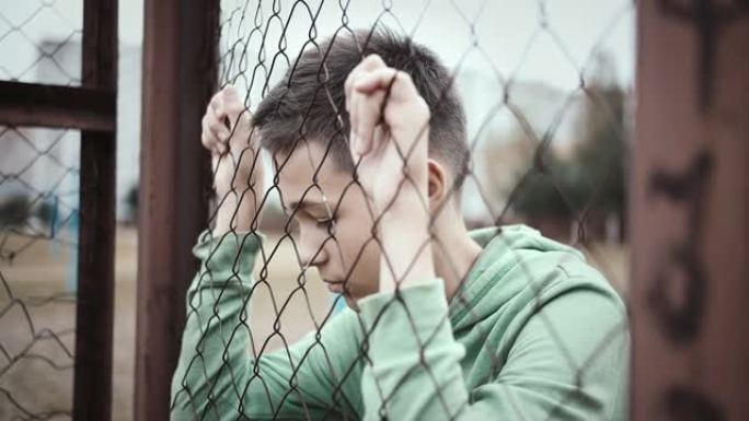 难民男孩独自一人低头在篱笆附近，沮丧的男孩垂下了眼睛，后悔了这一举动，电影拍摄