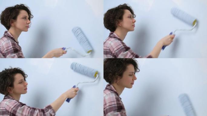 一个年轻的成年快乐的女人，用滚筒涂蓝色油漆。家庭房间公寓设计的维修和翻新。DIY修理房子。