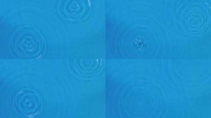 两滴雨落在蓝色的水中。顶视图。水滴落入水中，发散的水圈